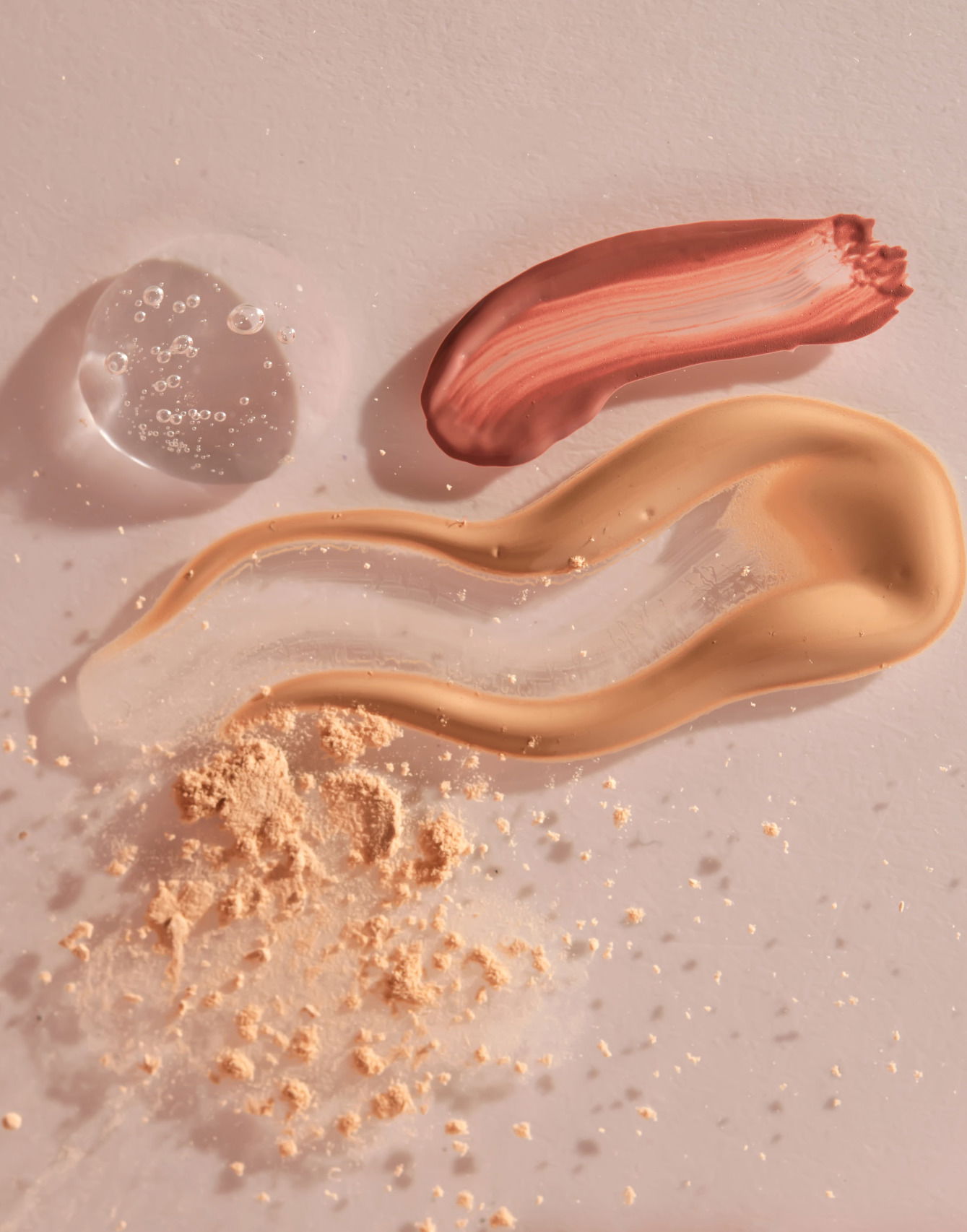 A sample of red lip gloss, foundation, powder and gel makeup base on a beige background. TikTok skin-friendly makeup