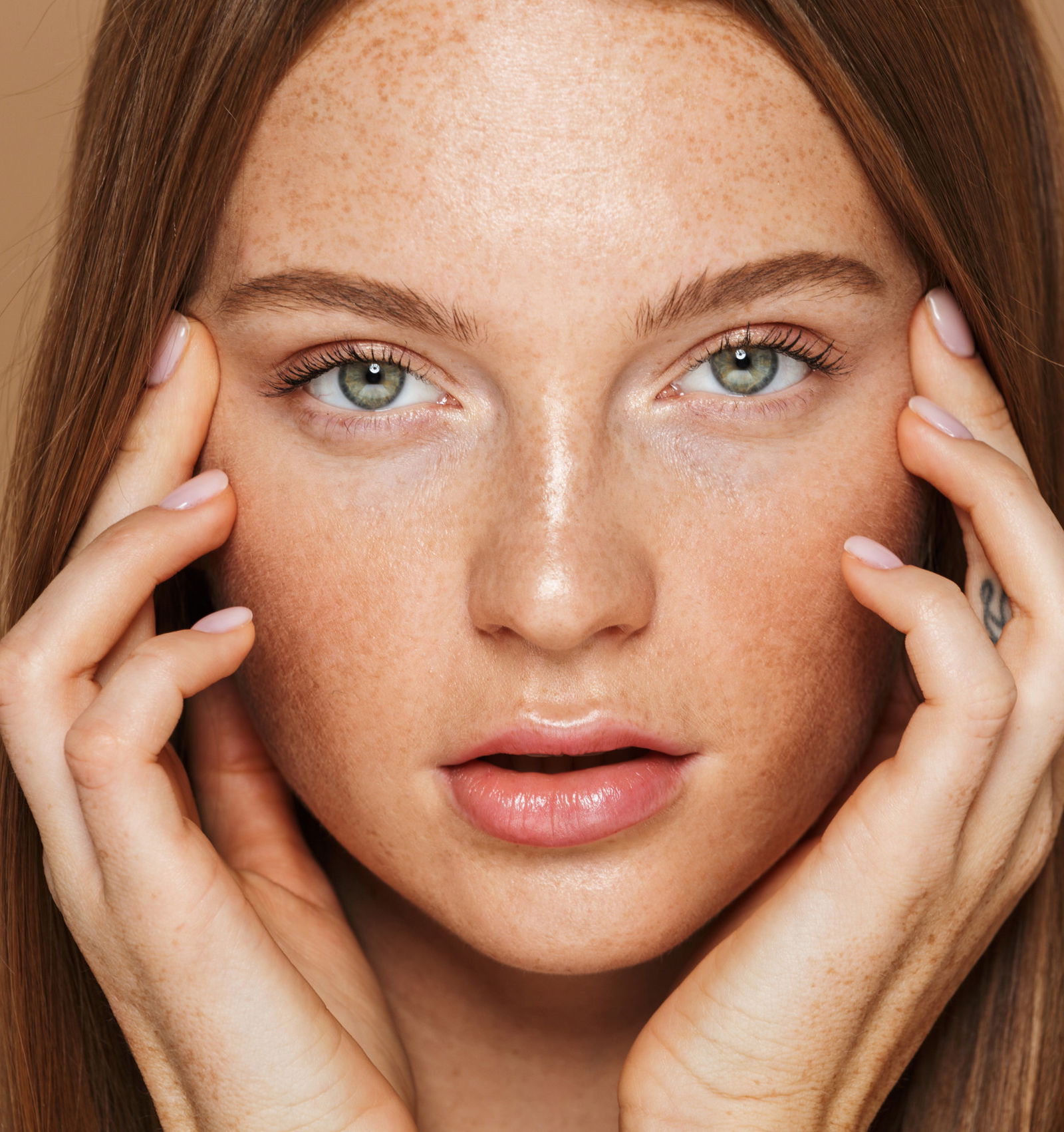 Beauty portrait of a sensual young topless woman with long red hair posing, holding hands at her face isolated over beige background workplace makeup women botox wrinkles 