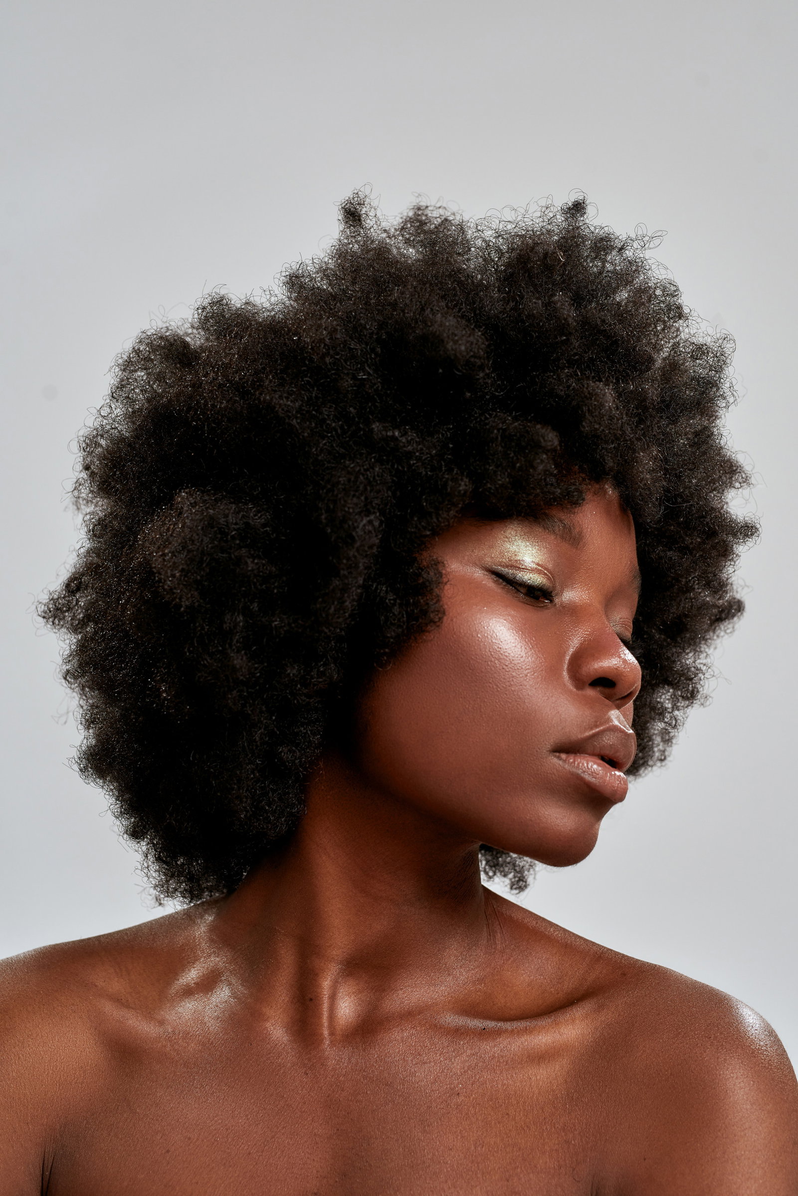 Portrait of beautiful african american female model with afro hair and perfect smooth glowing skin looking down posing isolated over gray background | Live That Glow Woman with a dark skin tone showing how to pick the perfect blusher