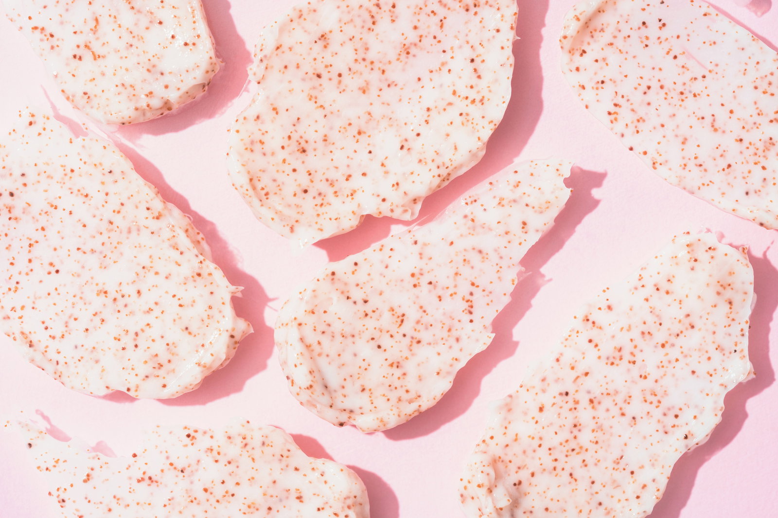 Many scrub smears over pink background Texture of body or face scrub - smudges with apricot and peach seeds Natural skincare product for exfoliating and peeling | Live That Glow Exfoliator to use before having a Brazilian wax or a bikini wax