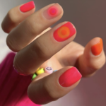 Close-up of a hand with neon pink and orange nails holding a small colorful beaded bracelet with smiley-face beads