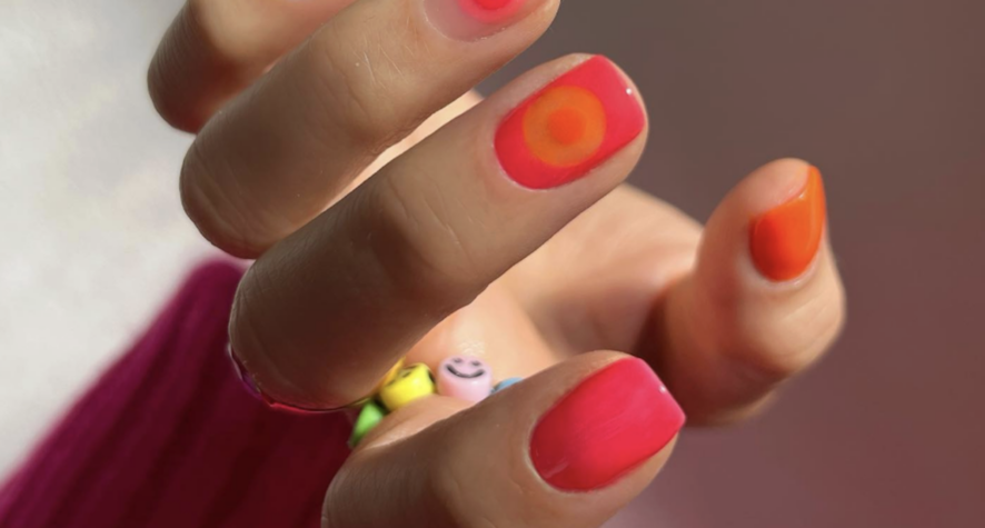 Close-up of a hand with neon pink and orange nails holding a small colorful beaded bracelet with smiley-face beads
