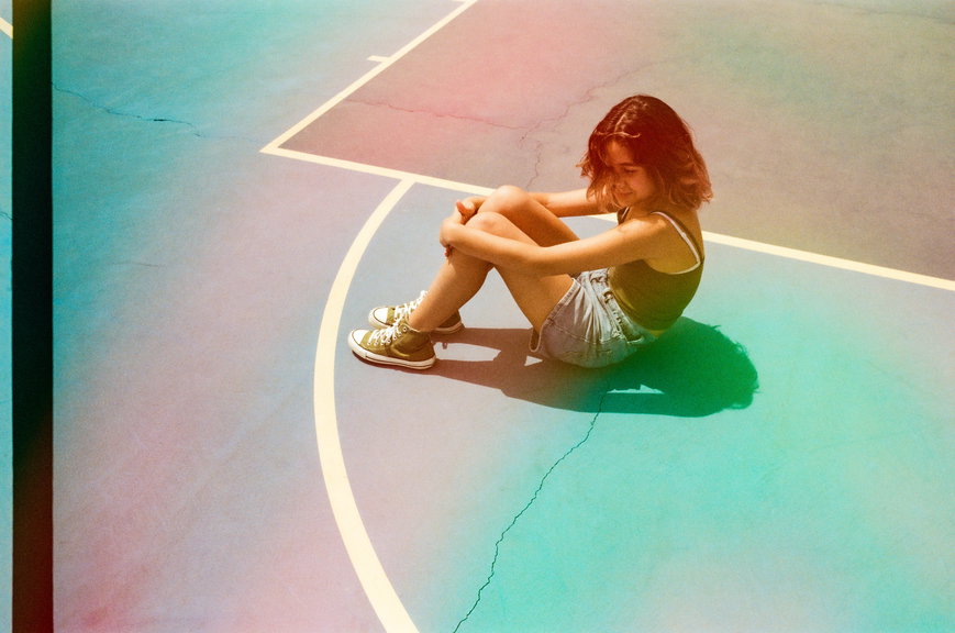Analog images of a teenager wearing shorts and a tank top standing or sitting in a basketball court. | Live That Glow beauty