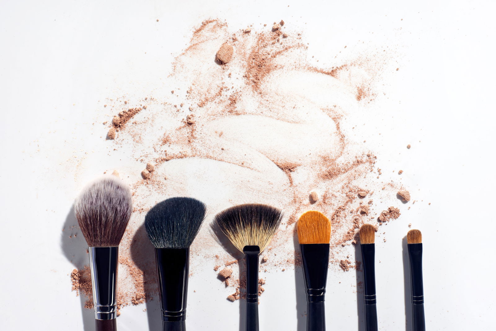 Set of brushes in a row on white background with scattered face powder