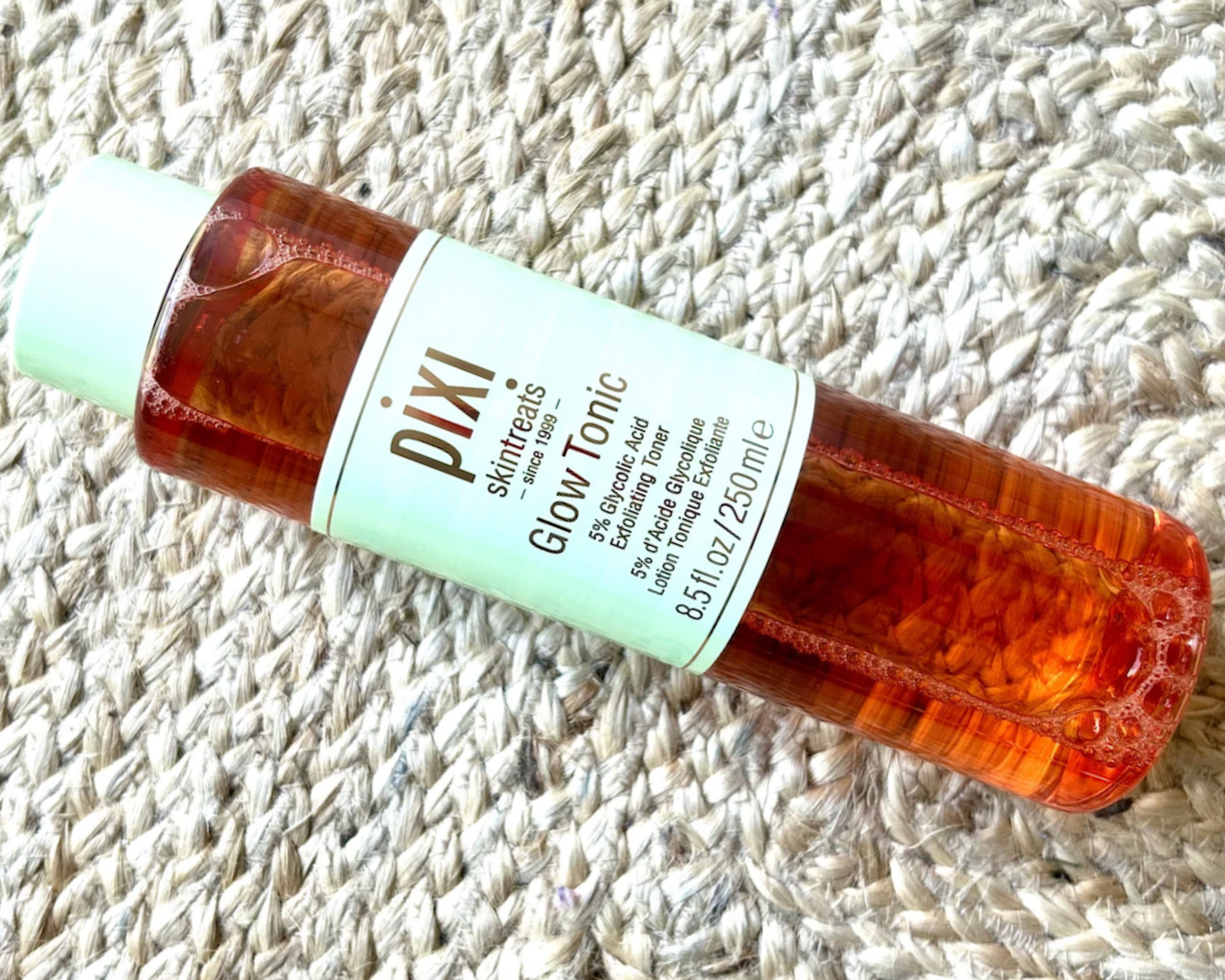 Pixi Glow Tonic 5% glycolic acid exfoliating toner bottle lying on a woven rug