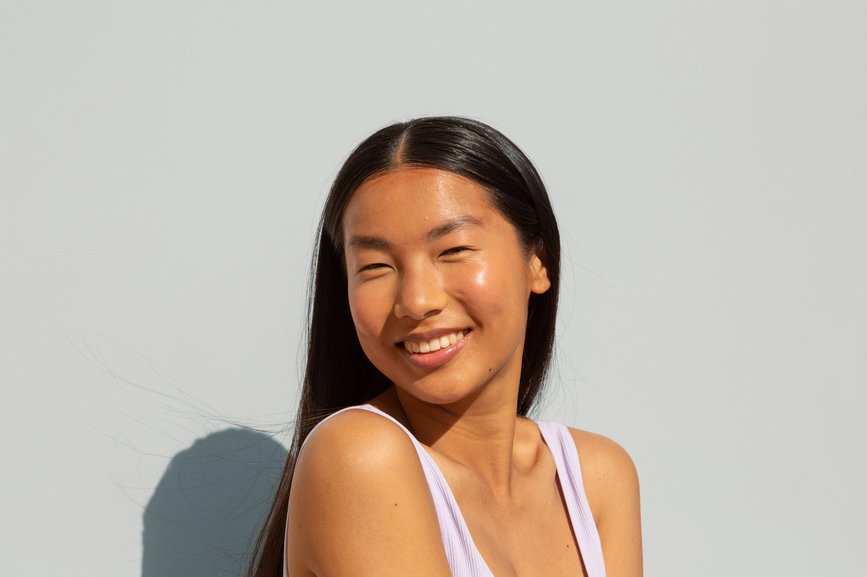 Happy woman with great positive energy. She is wearing a white bra and is enjoying the summer's sun. She is smiling and the portrait is shot against an isolated background. | Live That Glow