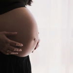 A pregnant woman in a black shirt and pants, against a white background.