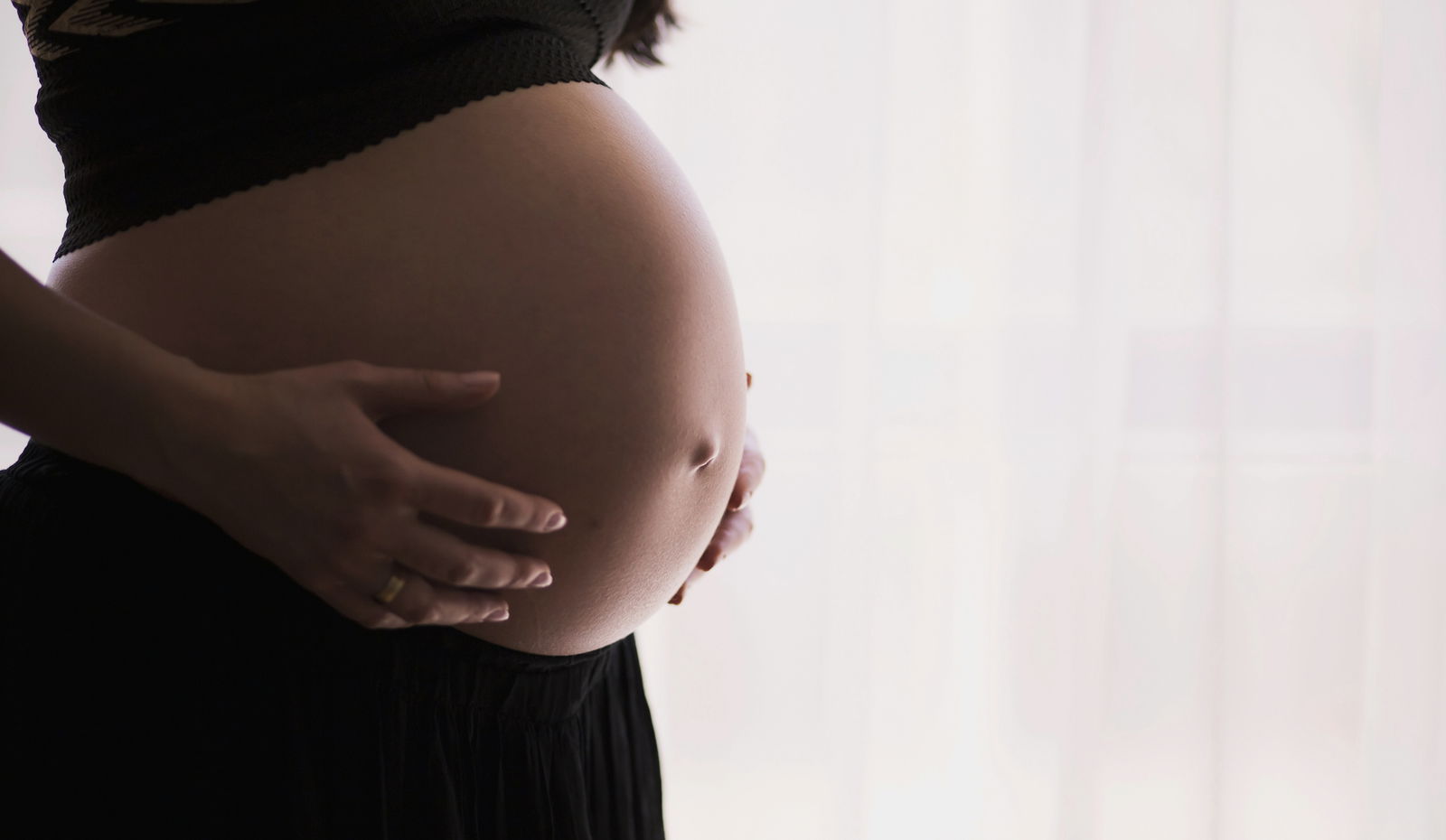 A pregnant woman in a black shirt and pants, against a white background.