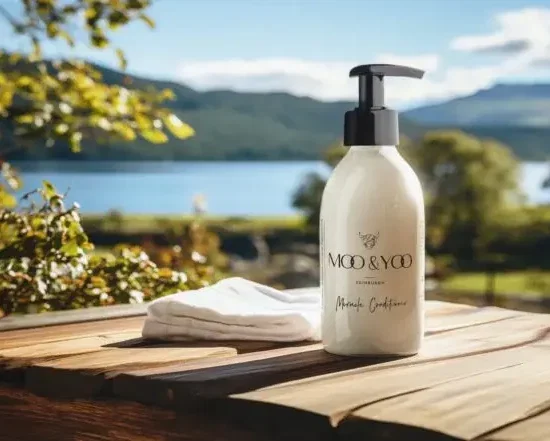 Cream pump bottle of MO&YO conditioner on a wooden table outdoors by a lake, with mountains in the background.