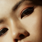 Close-up of a person’s face showing bold winged eyeliner and warm peach eyeshadow.