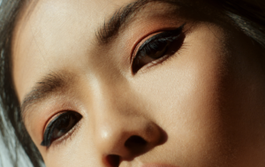 Close-up of a person’s face showing bold winged eyeliner and warm peach eyeshadow.