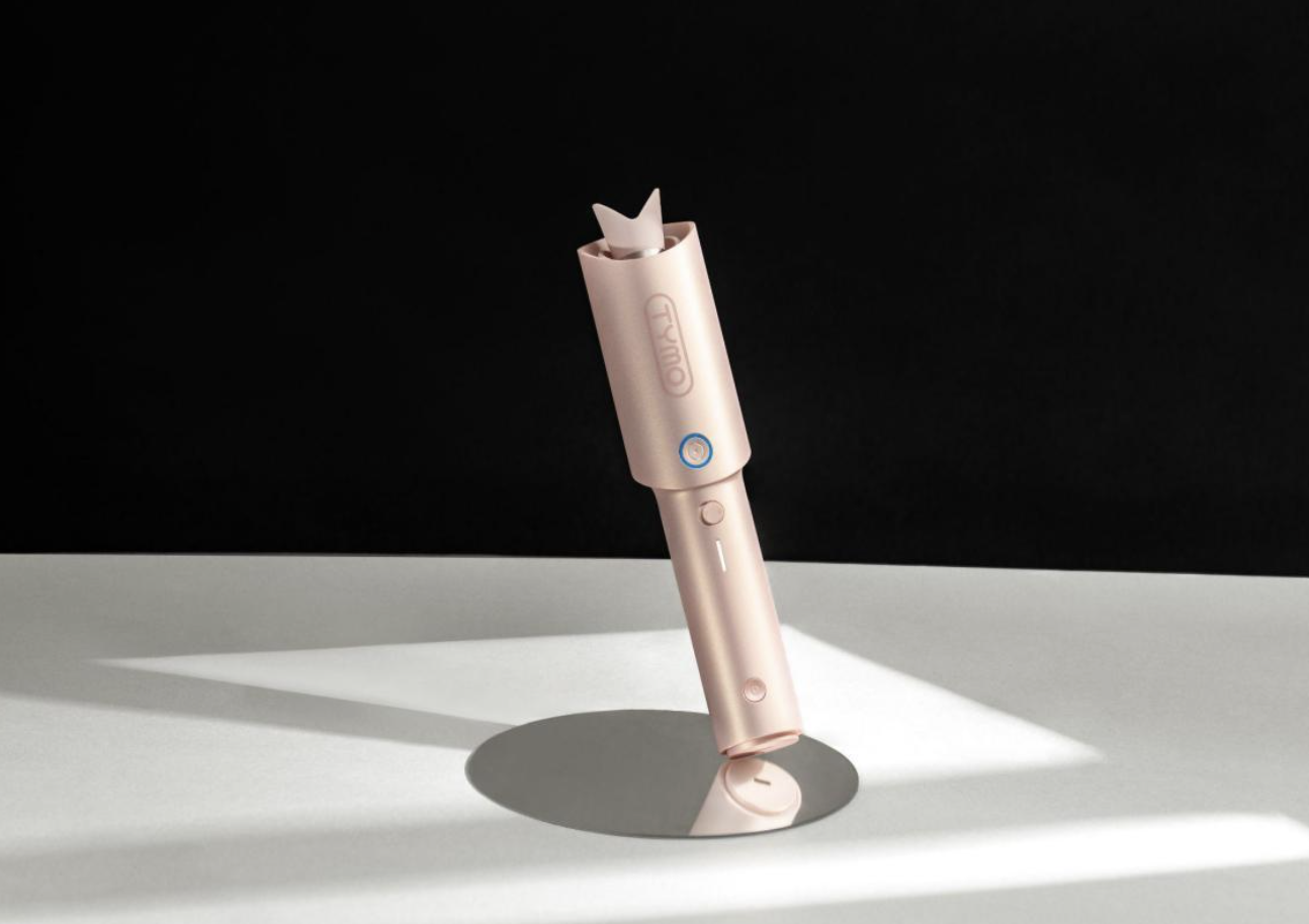 Rose-gold curling wand standing upright on a white surface with a soft shadow behind it.
