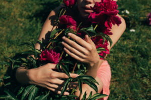 Person holding a vivid pink peony bouquet outdoors in a sunny garden.
