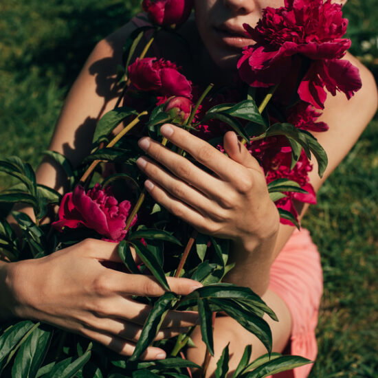 Person holding a vivid pink peony bouquet outdoors in a sunny garden.