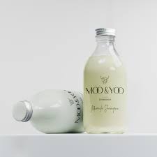 Two glass bottles of pale green beverage on a white surface, one upright and one lying on its side, with a labeled front showing the brand name.