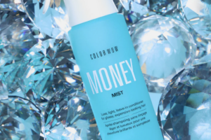 Blue Color Wow Money Mist spray bottle among sparkling blue crystal-like shapes, conveying a hair product advertisement