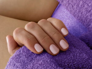 Close-up of a hand with pale pink manicured nails resting on a soft purple plush blanket.