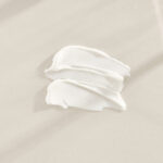 A smear of white cream spread on a pale beige surface or fabric area.
