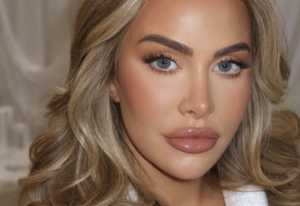 Close-up portrait of a woman with blue eyes, blonde wavy hair, and glossy nude lips.