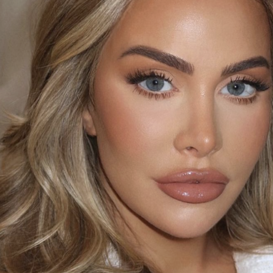 Close-up portrait of a woman with blue eyes, blonde wavy hair, and glossy nude lips.