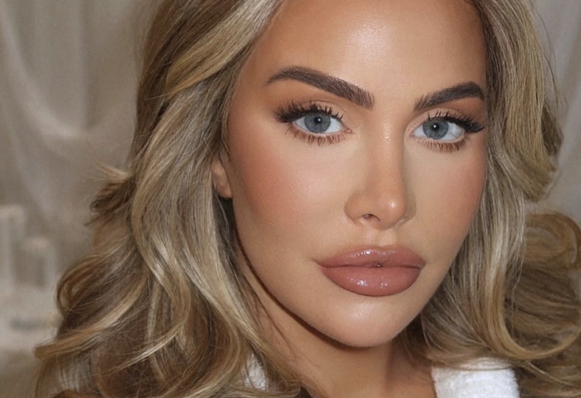 Close-up portrait of a woman with blue eyes, blonde wavy hair, and glossy nude lips.