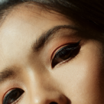 Close-up of a person’s eyes with orange eyeshadow and black eyeliner.
