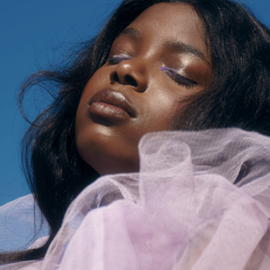 Portrait of a woman with eyes closed, wearing lavender tulle against a bright blue sky.