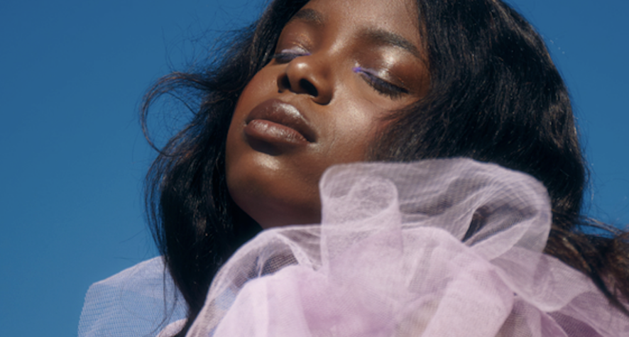 Portrait of a woman with eyes closed, wearing lavender tulle against a bright blue sky.