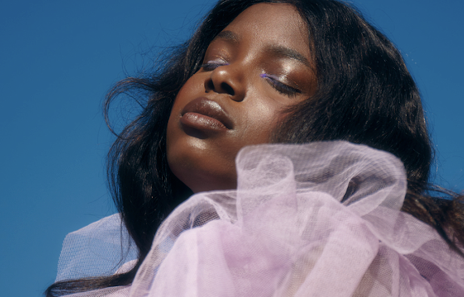 Portrait of a woman with eyes closed, wearing lavender tulle against a bright blue sky.