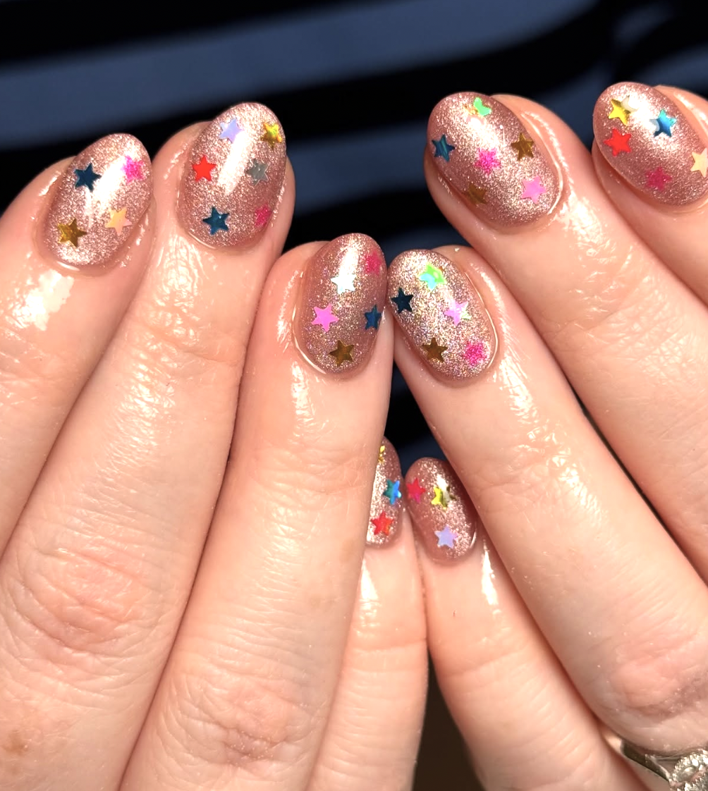 Close-up of hands with glittery pink nails and multicolored star-shaped decals