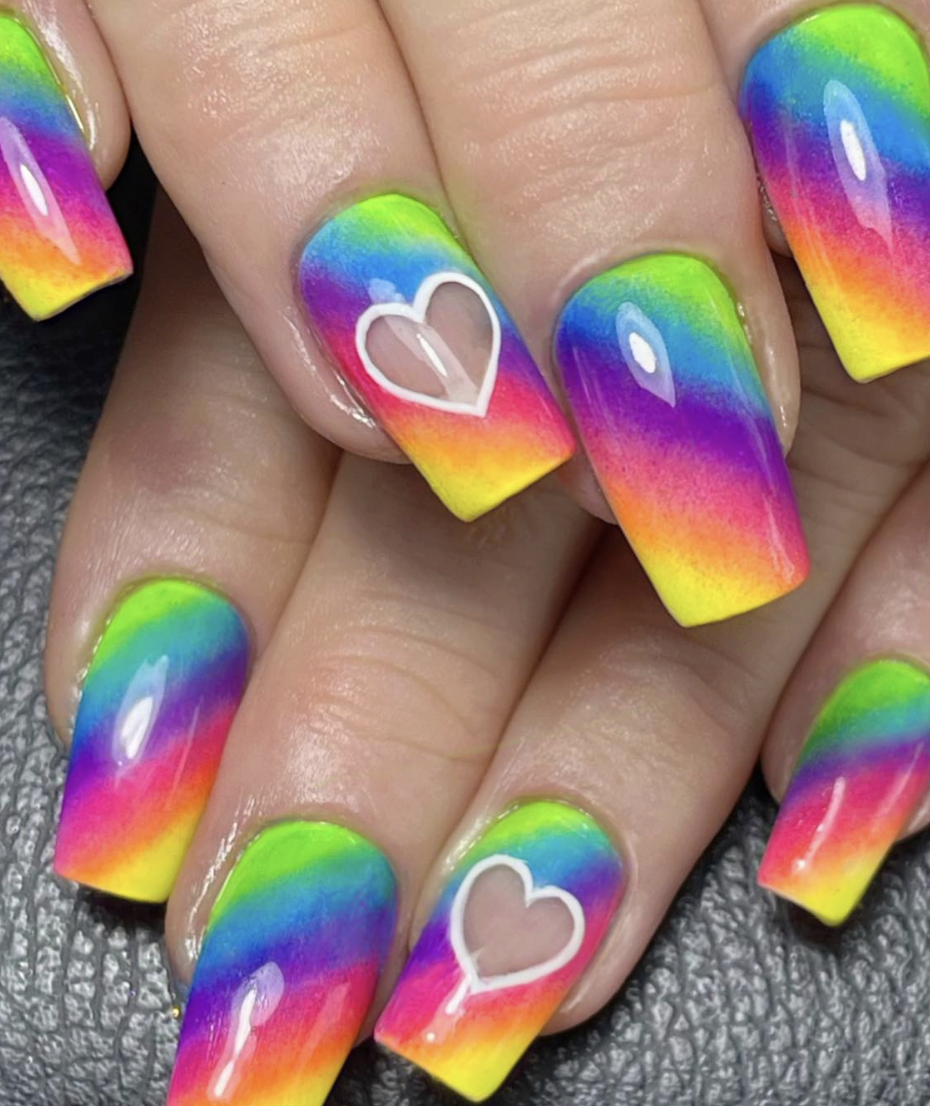 Nail art with a bright rainbow gradient on long square nails and white heart cutouts on a few nails.