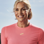 Smiling woman in a pink athletic shirt outdoors under a blue sky.