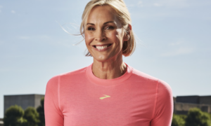 Smiling woman in a pink athletic shirt outdoors under a blue sky.