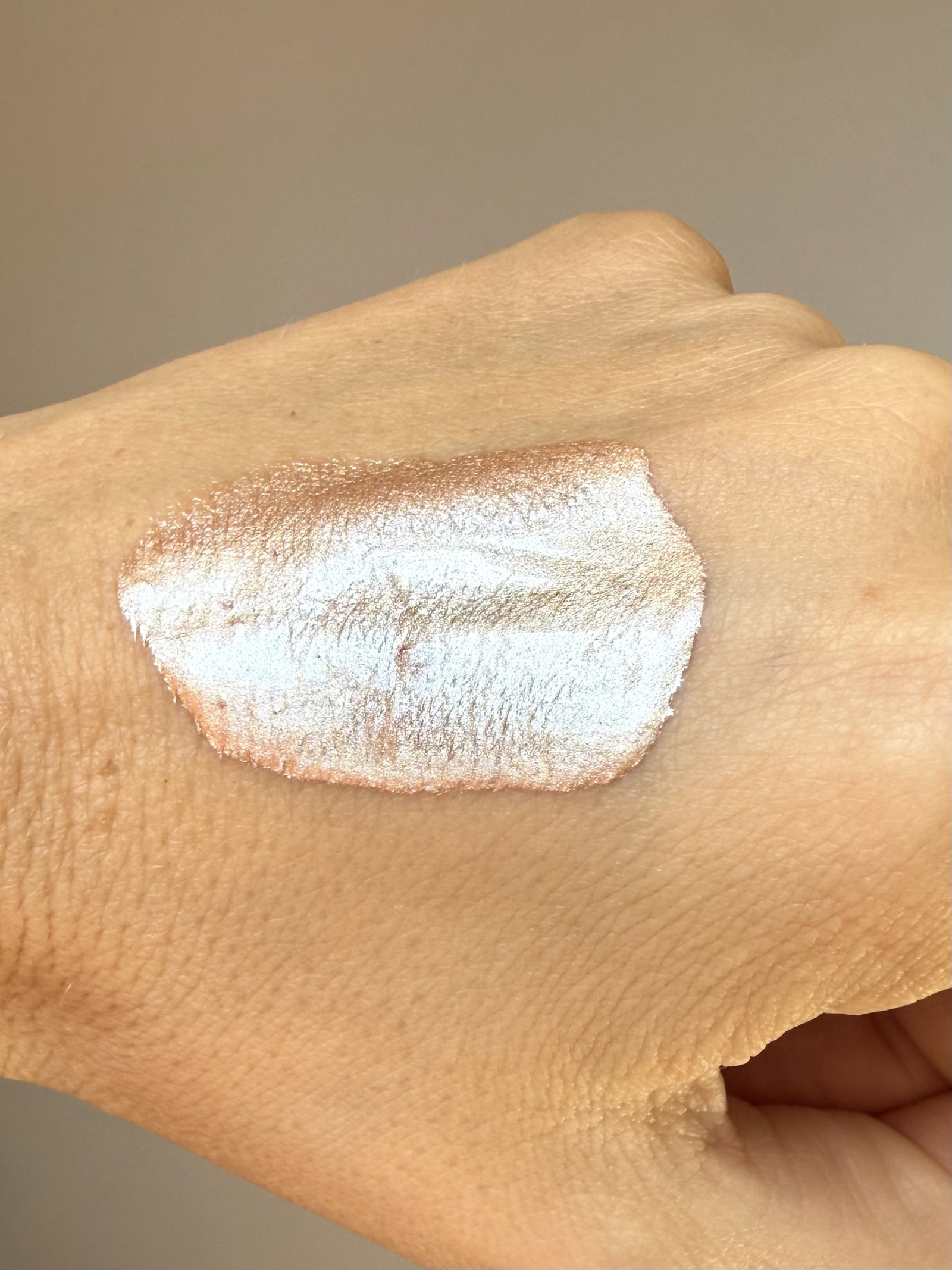Close-up of a hand showing a shimmery peach-silver eyeshadow swatch on the skin.