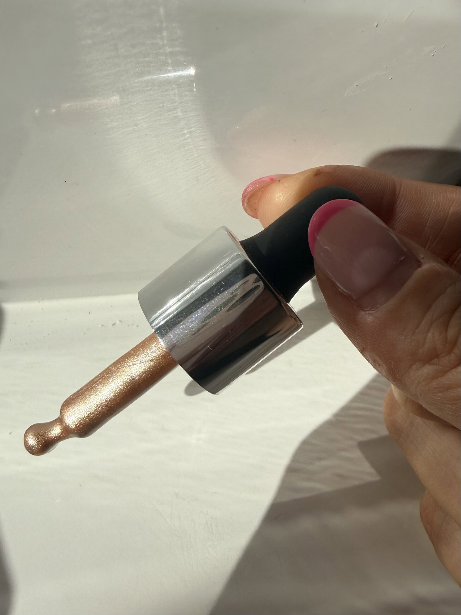 Close-up of the ICONIC London Illuminator dropper applicator coated in champagne-gold liquid highlighter, photographed in natural sunlight.