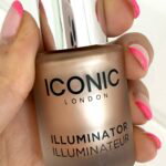 ICONIC London Illuminator in the shade Original held in hand, showing the frosted glass bottle, silver cap and black dropper applicator.