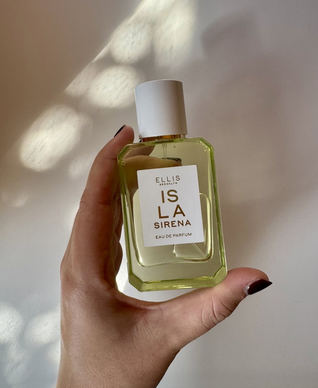 Ellis Brooklyn Isla Sirena eau de parfum bottle held in hand against a softly lit neutral background.