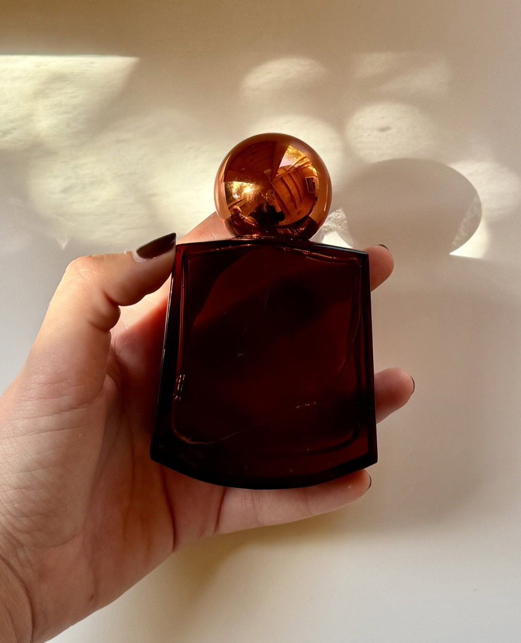 Pleasing Welcome Dreams perfume bottle with amber glass and spherical cap held in hand in warm sunlight.