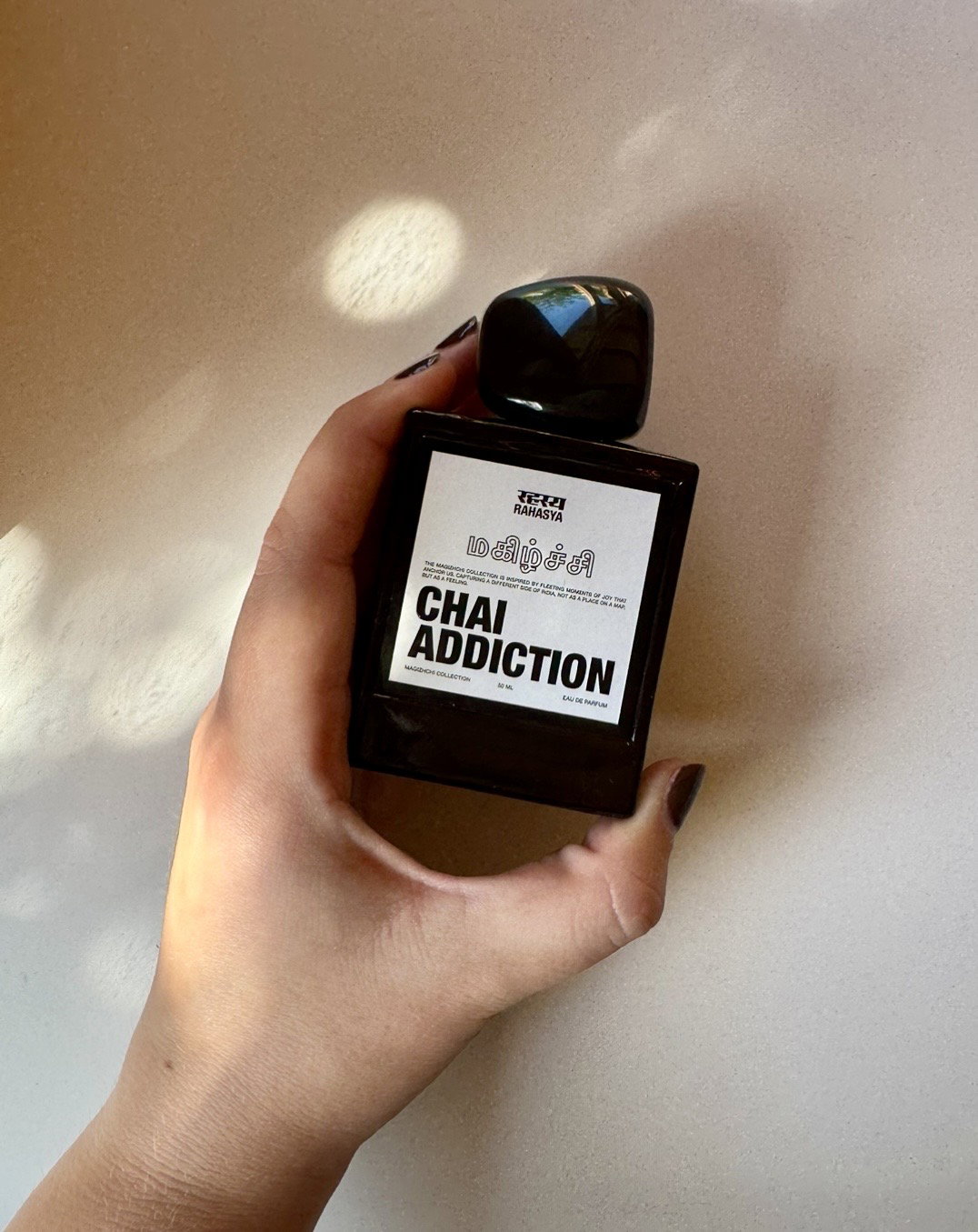 Rahasya Chai Addiction eau de parfum bottle held in hand against a softly illuminated neutral background.
