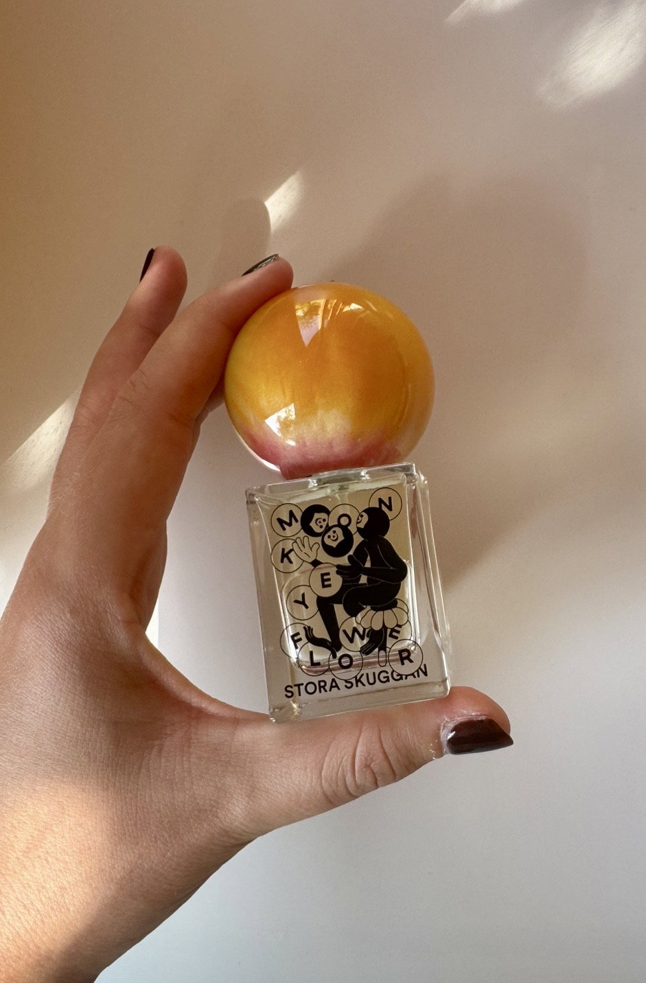 Stora Skuggan Monkey Flower perfume bottle with sculptural marbled cap held in hand in natural sunlight.