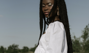 Young woman with long braids wearing a white off-shoulder blouse outdoors on a sunny day.