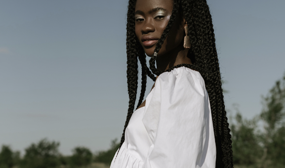 Young woman with long braids wearing a white off-shoulder blouse outdoors on a sunny day.