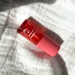 Close-up of a pink/red cosmetic bottle resting on a soft white towel.