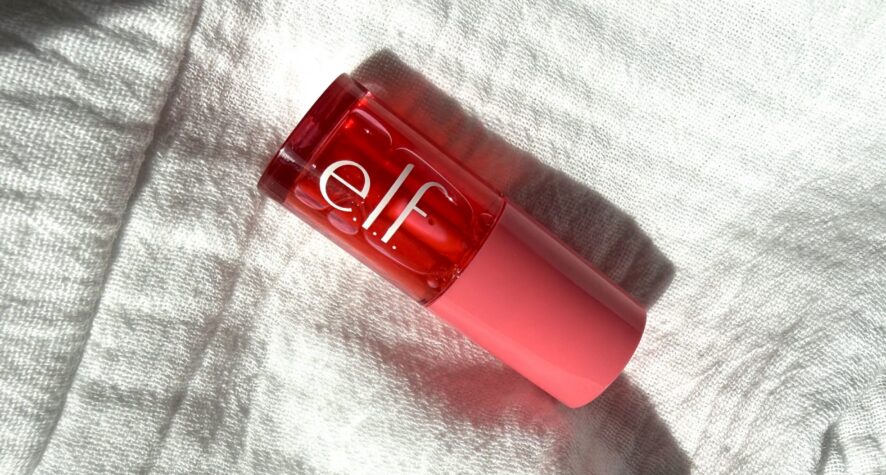 Close-up of a pink/red cosmetic bottle resting on a soft white towel.