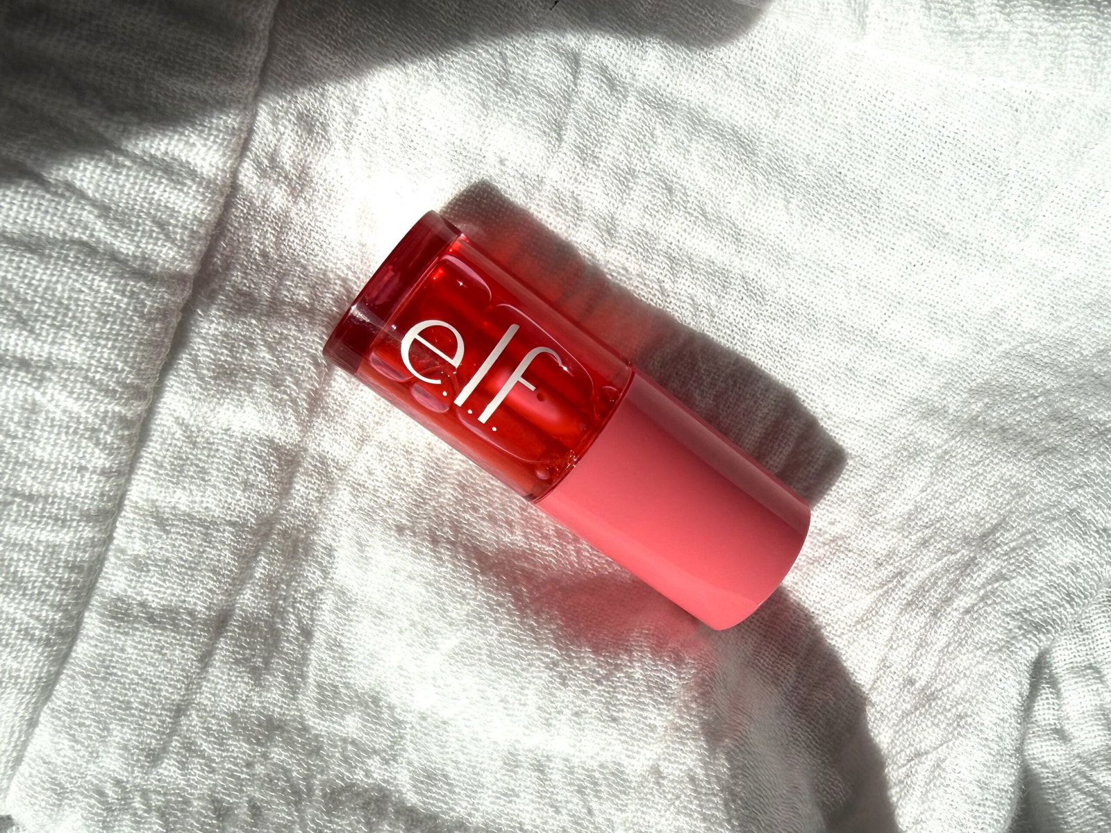 Close-up of a pink/red cosmetic bottle resting on a soft white towel.