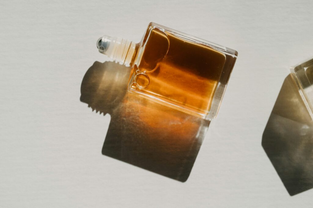 A square glass bottle with amber-brown liquid lies on its side, casting a dark shadow on a light surface.