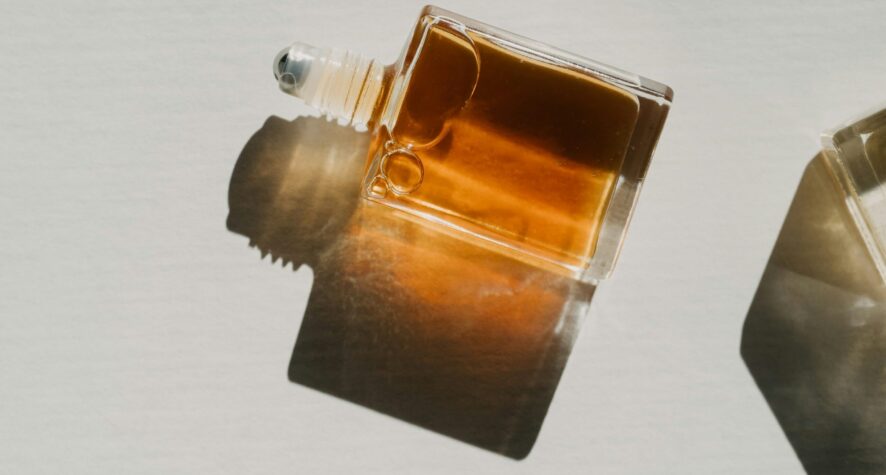 A square glass bottle with amber-brown liquid lies on its side, casting a dark shadow on a light surface.