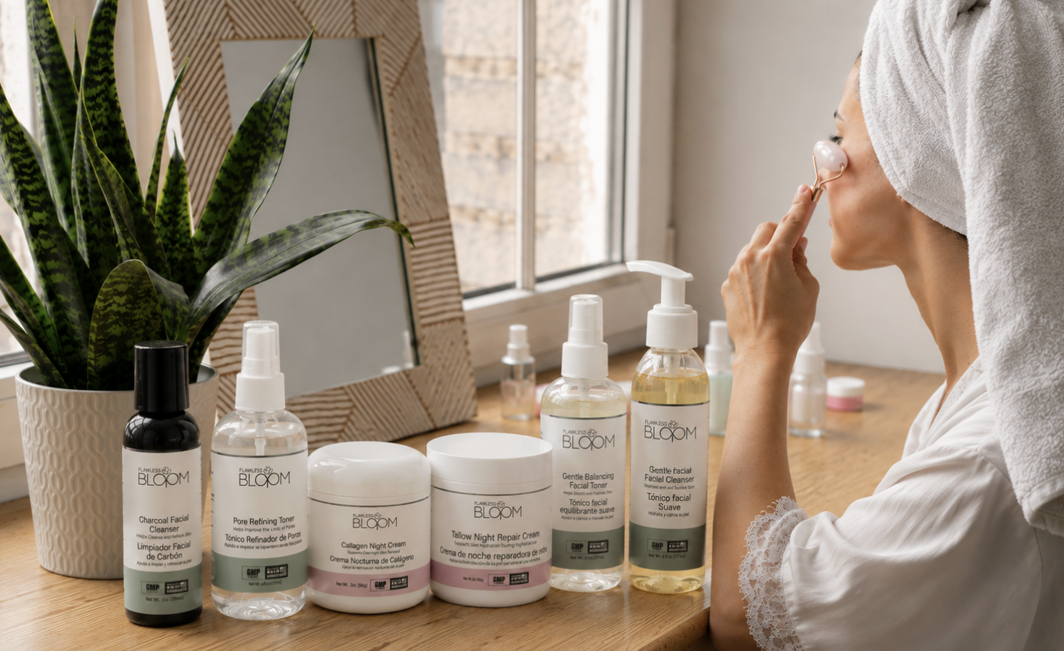 Woman with a towel wrapped around her head applies a facial patch while seated at a wooden vanity with BLOOM skincare bottles nearby.