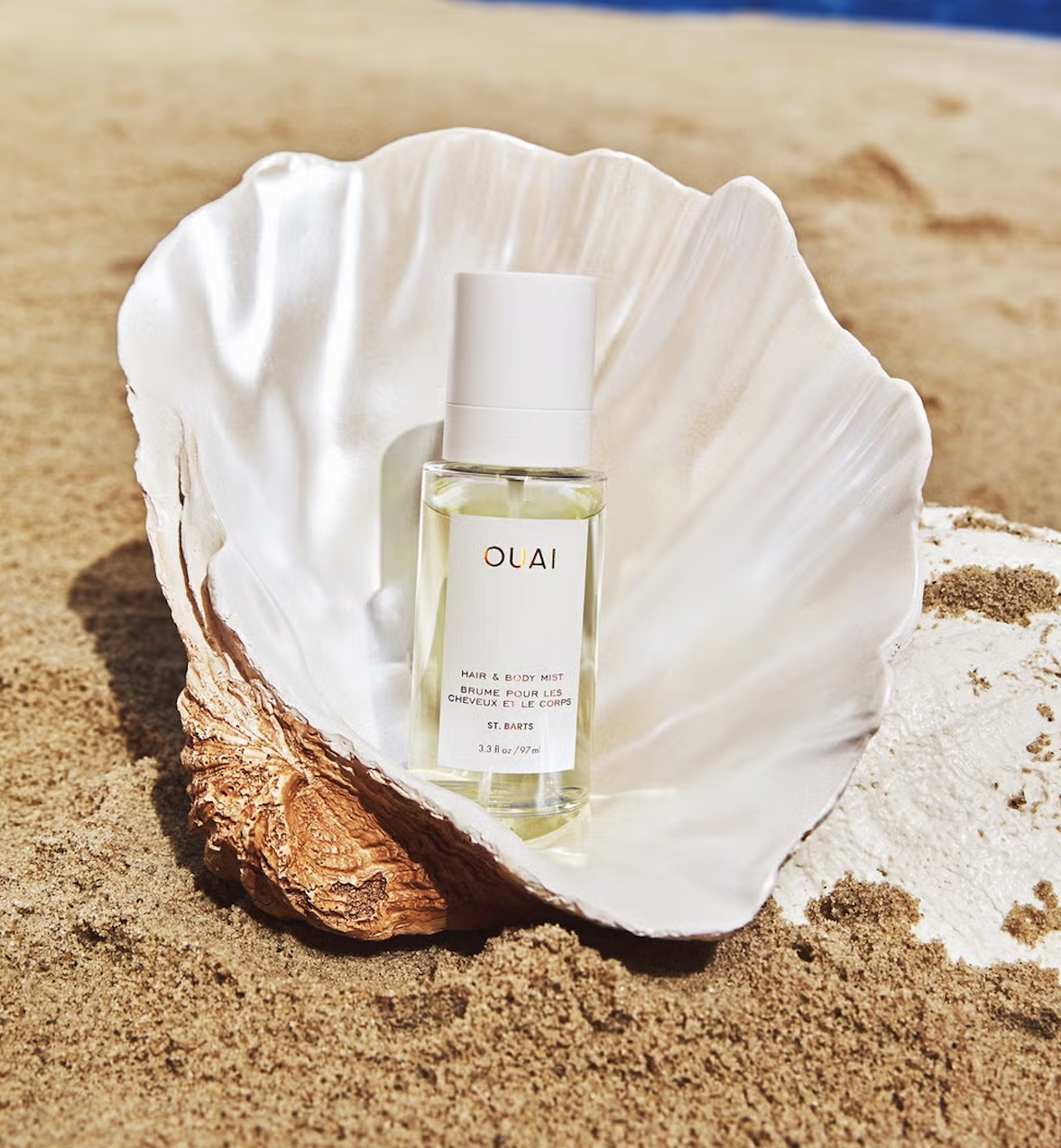 ouai-st-barts-hair-body-mist | Live That Glow OUAI St. Barts Hair and Body Mist photographed in a seashell on the beach