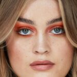 Woman wearing bold orange-red eyeshadow with glossy, softly waved hair.